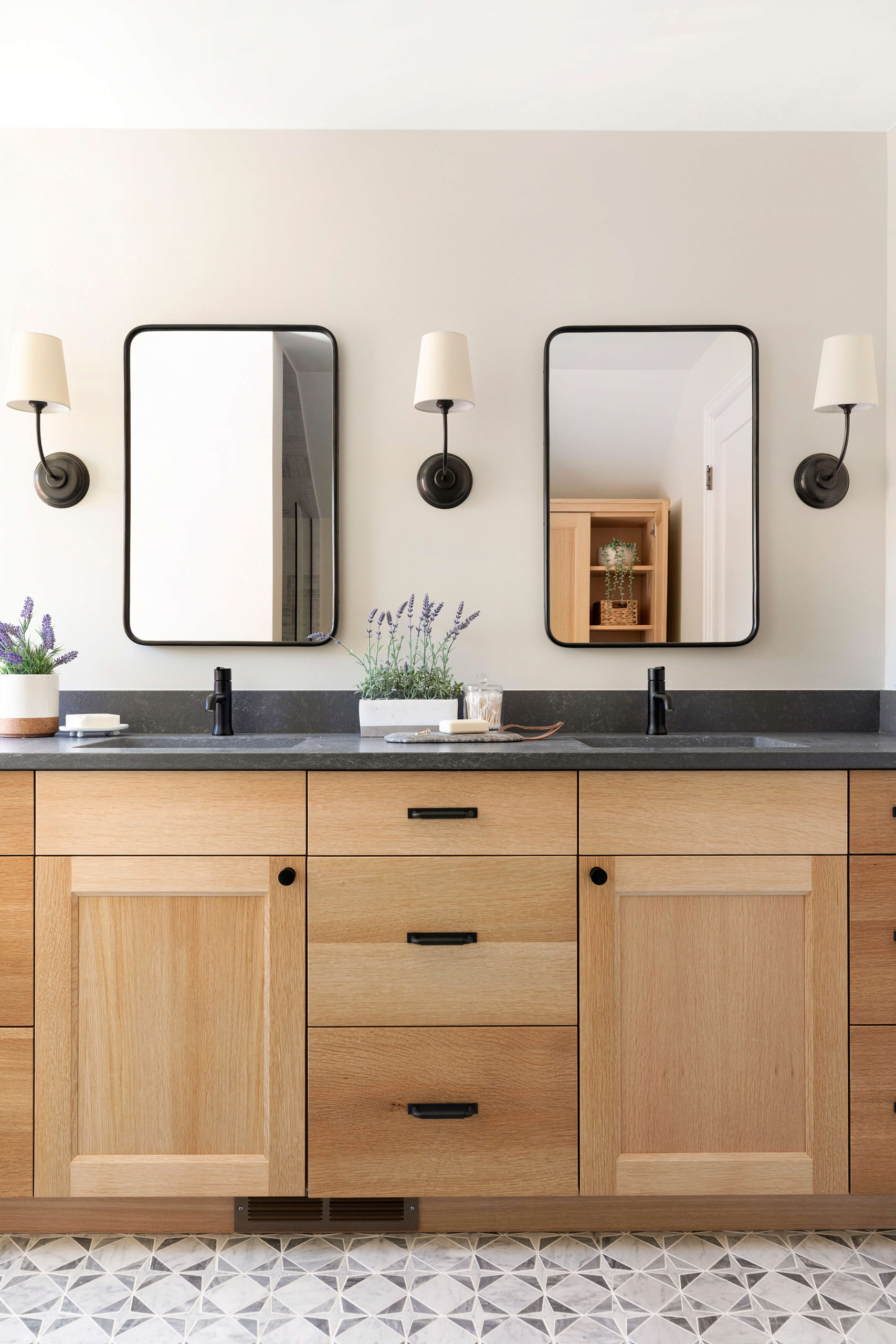 Primary owners bathroom white oak vanity with black quartz countertop, marble mosaic floor tile, black single handle faucet, black wall sconces, black wall vanity pivot mirrors, black vanity cabinet hardware