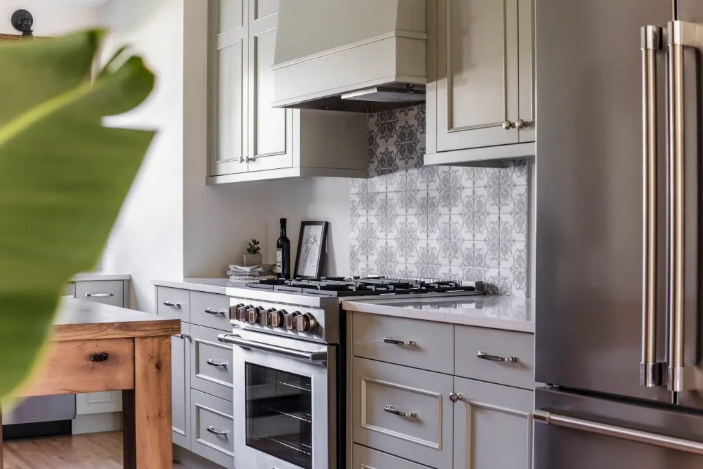Custom kitchen cabinetry and range hood with soft green cabinets, polished nickel cabinet hardware pulls, hand made backsplash tile