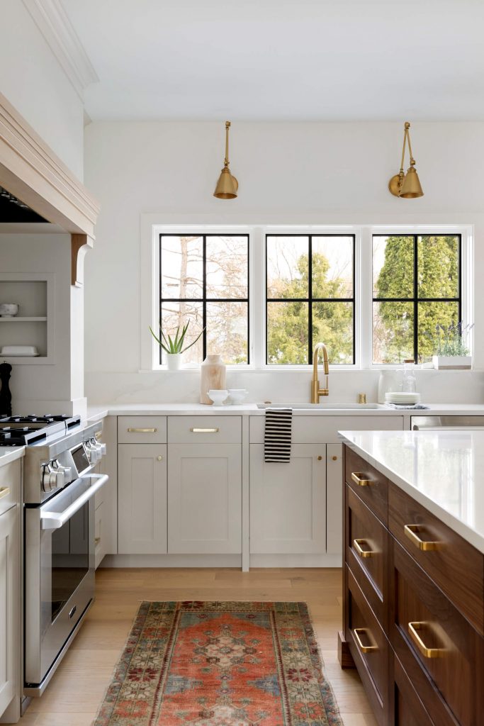 Custom kitchen cabinetry with black grid windows, brass wall sconces and sink faucet with walnut island