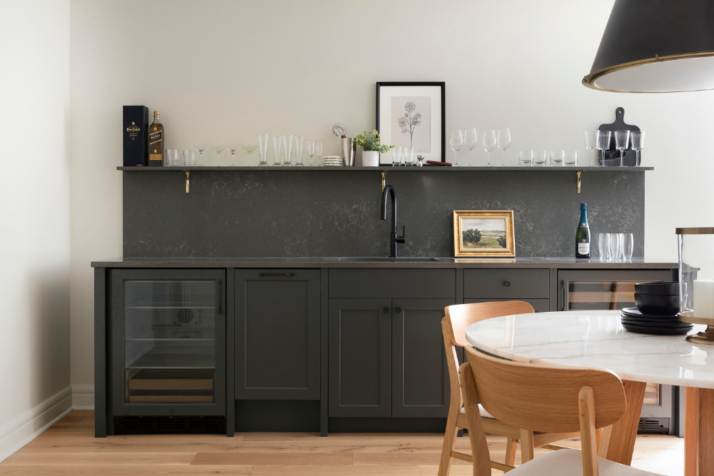 Dark gray wet bar with quartz backsplash, display shelf, and paneled appliances.