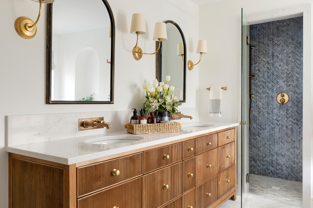 Primary bathroom with white oak reeded vanity, brass hardware, and arched mirrors.