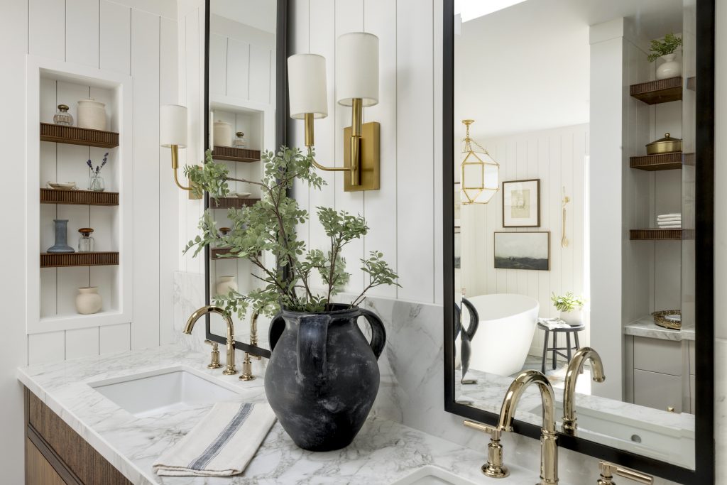 Bathroom vanity with brass wall sconces, tall vanity mirrors, polished gold brass plumbing fixtures, quartz countertops and tall backsplash, walnut reeded vanity, walnut reeded shelves in well designed accessory niche