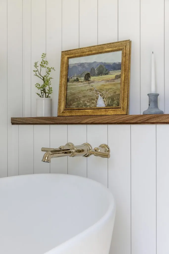 Shiplap paneled walls, walnut open shelving and polished brass tub filler