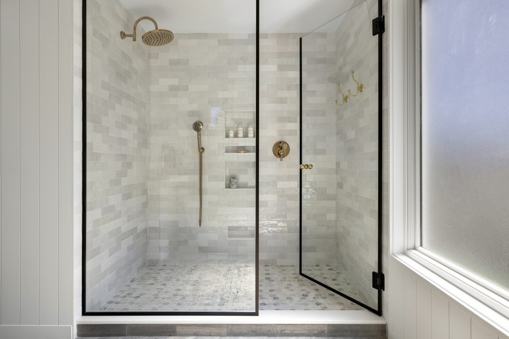 Spacious walk in shower with 3x8 ceramic tiles and polished brass fixtures.
