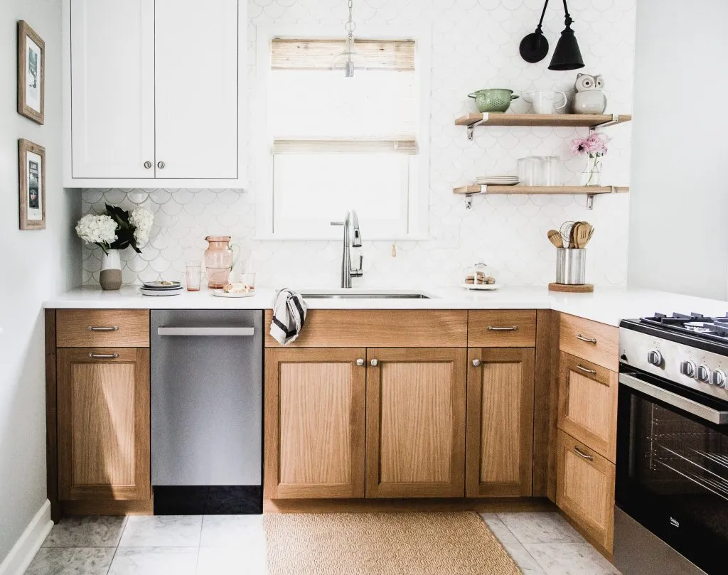 Custom cabinetry with white oak lower cabinets and white upper cabinets with a white fishscale backsplash tile and floating shelves with black sconce, range in peninsula