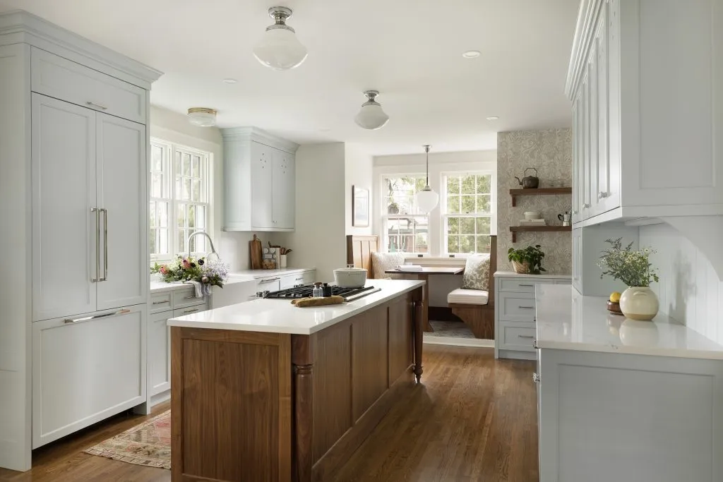 Colonial kitchen design with walnut island and light blue custom cabinetry with vintage lighting and semi-flush mounts over island, integrated built-in appliances, farmhouse apron sink