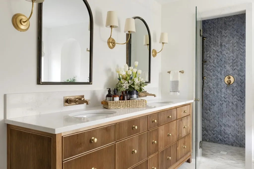 Custom double bathroom reeded front vanity in primary owners suite with wall mount faucet, arched mirror and quartz countertops