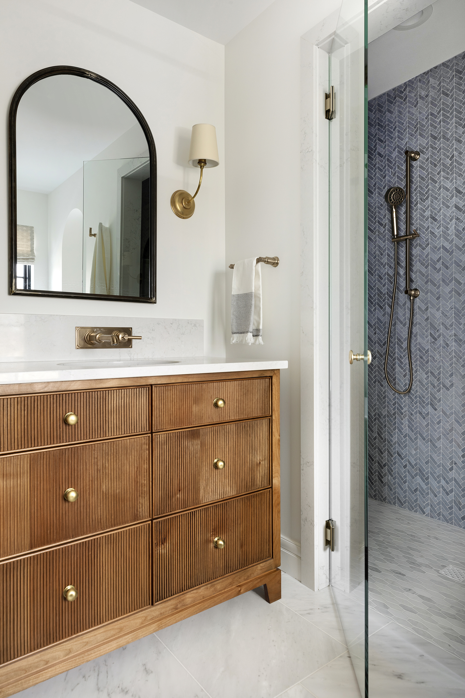 Custom double bathroom reeded front vanity in primary owners suite with wall mount faucet, arched mirror and quartz countertops