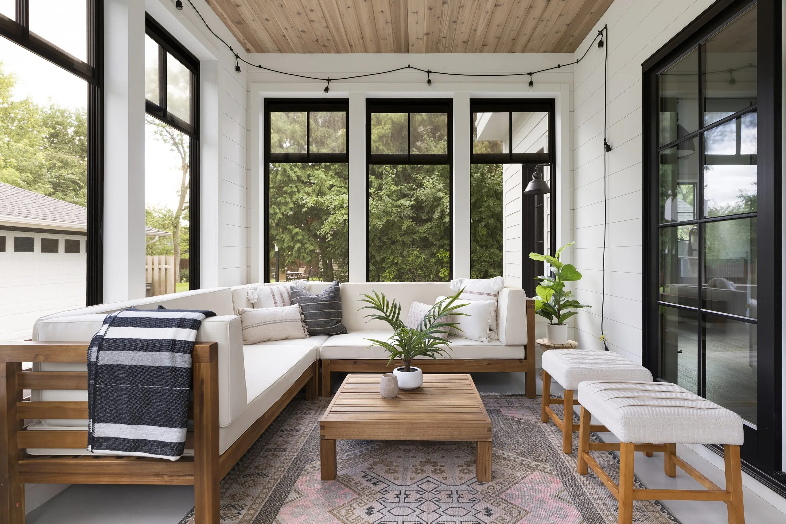 Screen porch, white cushion furniture with teak/wood frame and colorful rug.