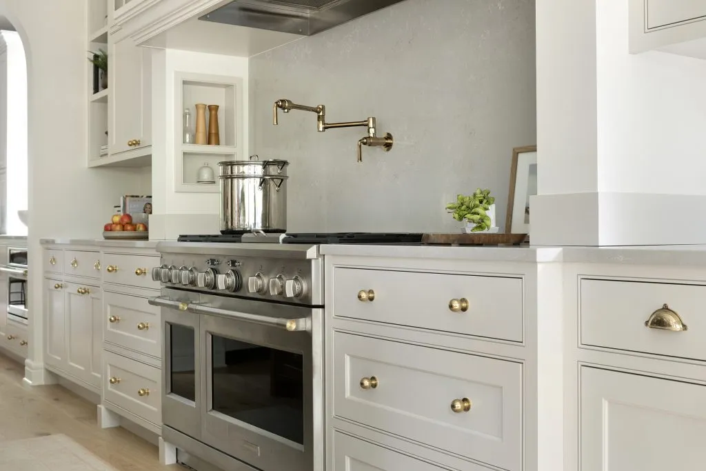 Range hood alcove with 48 inch range and polished gold pot filler over quartz backsplash, custom cabinetry and alcove niches