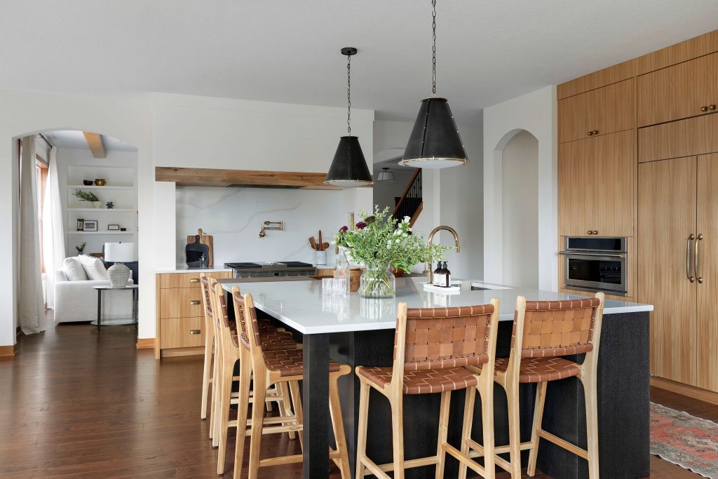 Custom quartered red elm veneer cabinetry kitchen with double sided black white oak island, black pendant lights, alcove range hood with quartz backsplash and brass pot filler, leather counter stools, engineered hardwood floors