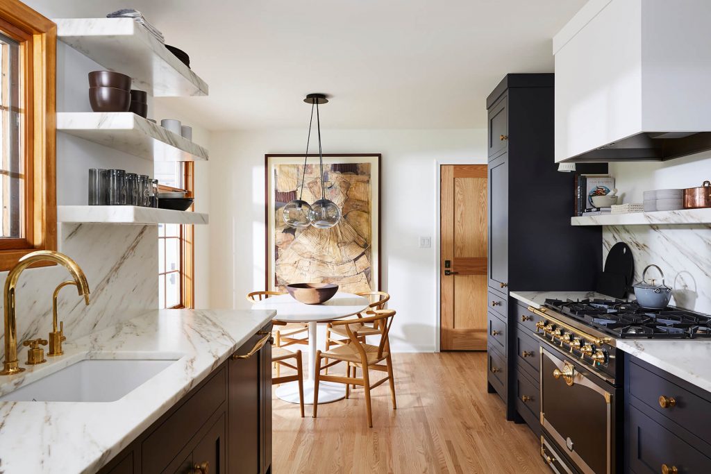 Moody black custom cabinetry, burnished brass cabinet hardware, floating marble shelves and French cooking range.