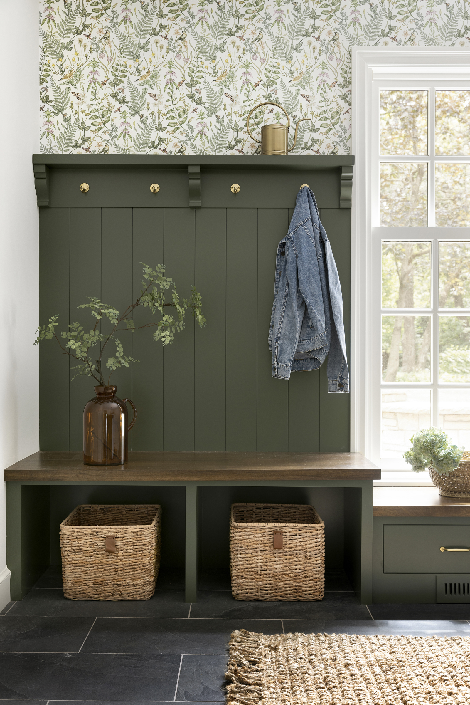 Painted green mudroom cabinetry, whimsical wallpaper and aged brass hardware.