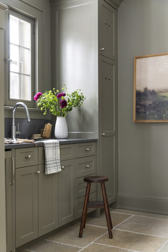 Olive green tone mudroom with drop zone, hand washing station and decorative peg hooks.