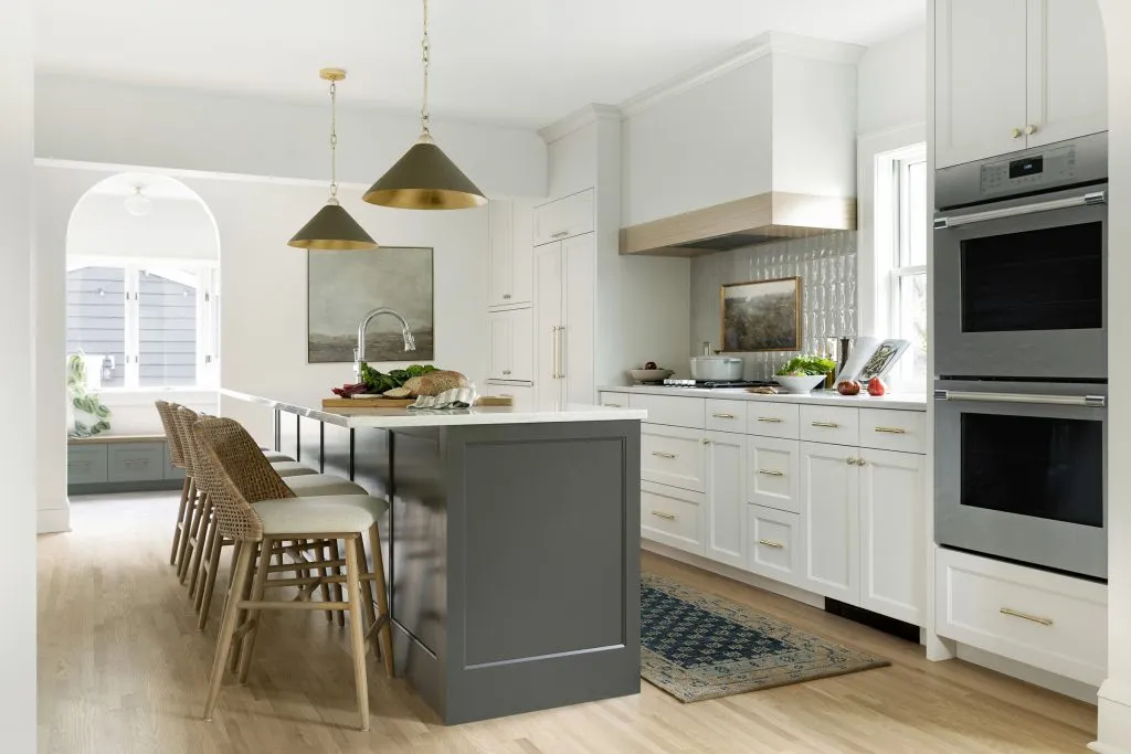 How to Refresh a 1920s Home, While Mixing Modern and Traditional Design Styles. Natural red oak floors, off white cabinetry with dark painted island, apron sink with stone drip ledge and mixed metals.