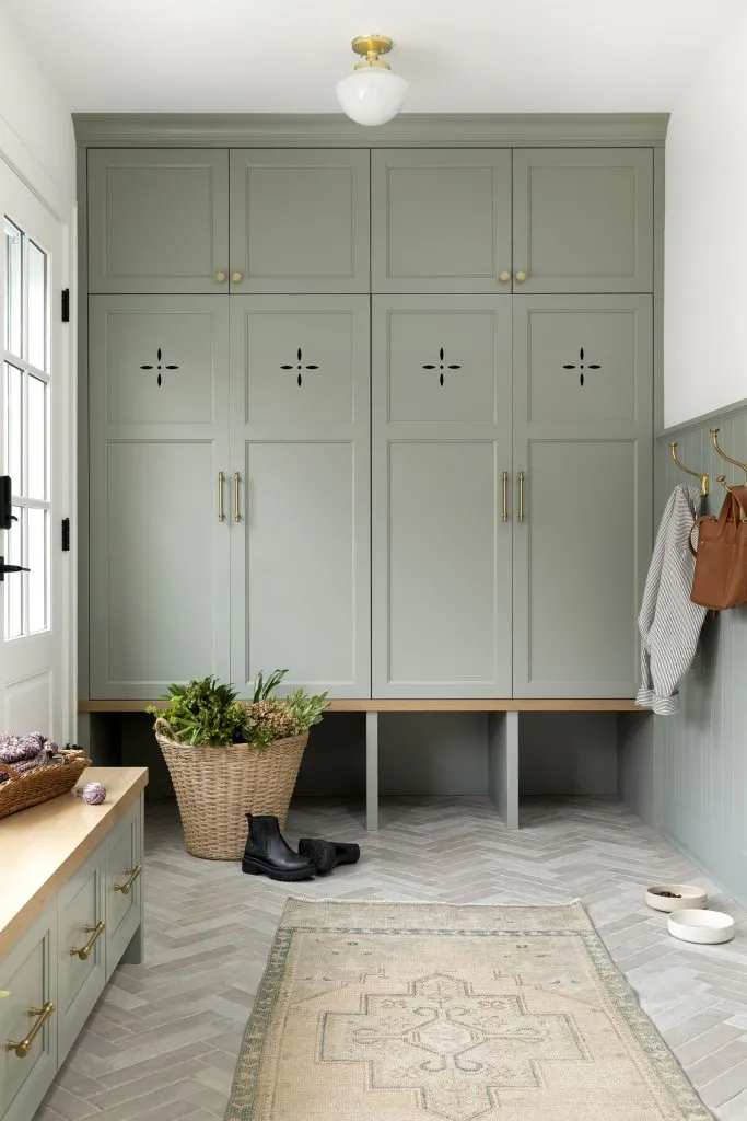 How to Refresh a 1920s Home, While Mixing Modern and Traditional Design Styles. Soft green-blue painted mudroom cabinetry with ventilation holes, and white oak bench.