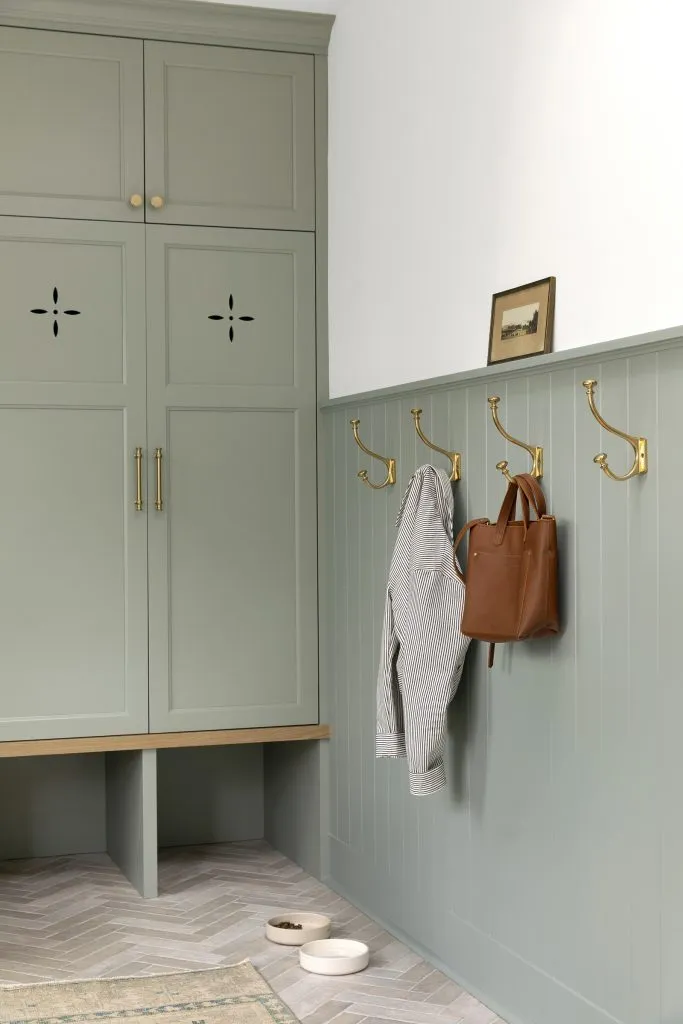 How to Refresh a 1920s Home, While Mixing Modern and Traditional Design Styles. Soft green-blue painted mudroom cabinetry with ventilation holes, and white oak bench.