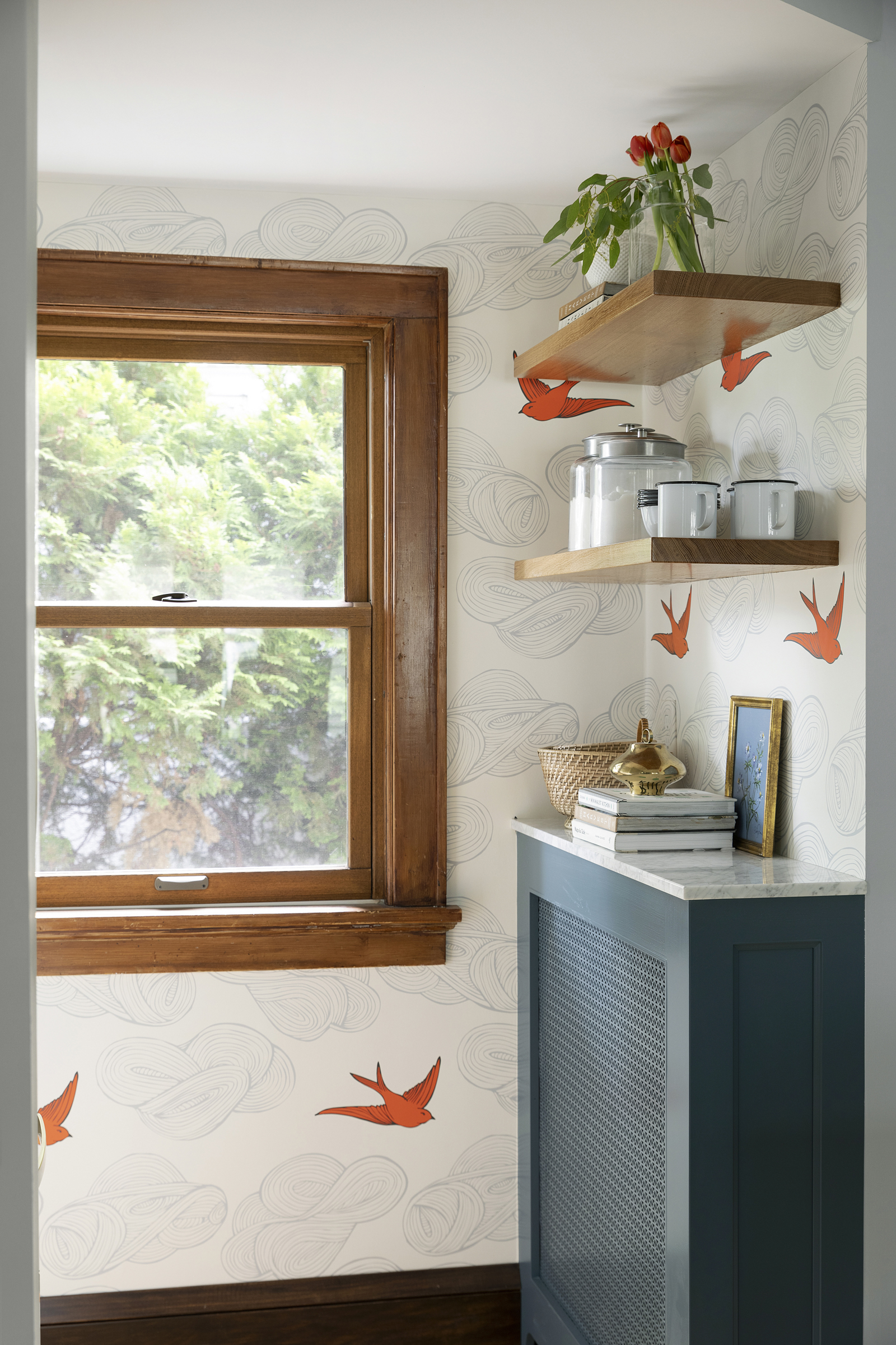 Cozy kitchen nook with custom blue radiator cover, orange bird wallpaper and wood shelving