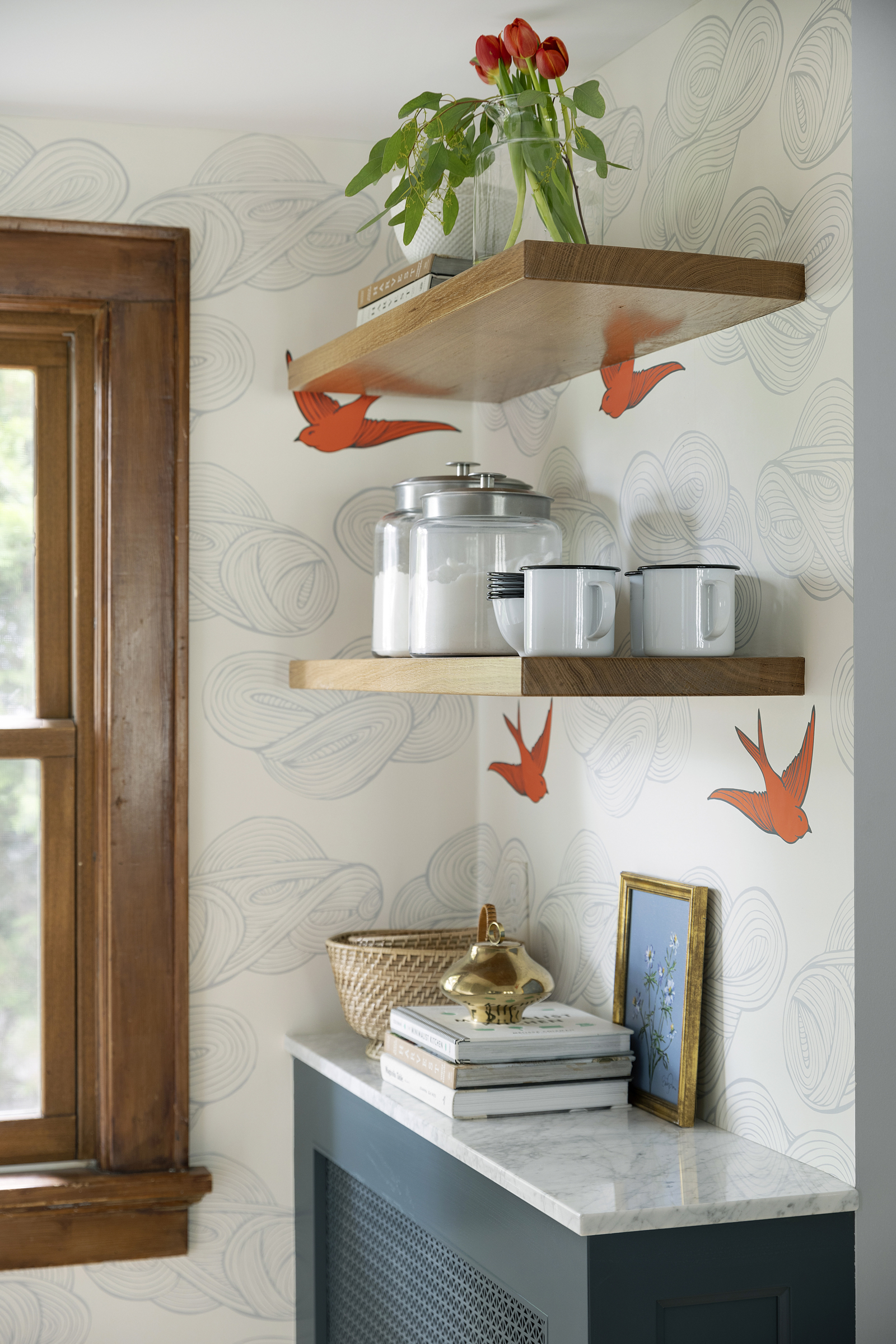 Cozy kitchen nook with custom blue radiator cover, orange bird wallpaper and wood shelving