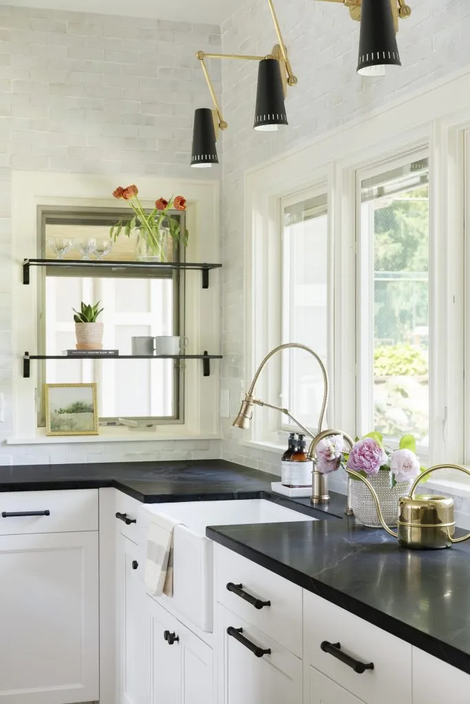 Custom kitchen renovation featuring double white oak islands with overhead brass linear chandeliers and natural quartzite countertops, white perimeter custom cabinetry with natural soapstone countertops, black cabinet hardware and custom plaster range hood.
