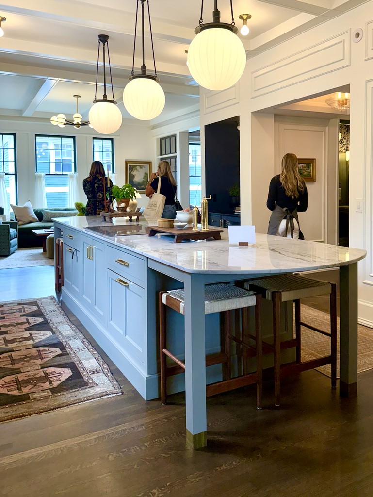 A modern kitchen with a marble island, pendant lights, and three women standing and talking. The space is bright with large windows and contemporary decor, inspired by Seven Things We Brought Home from Jean Stoffer’s Kitchen Collection.